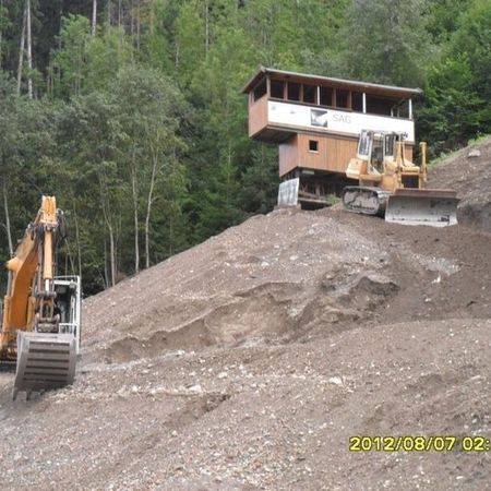 Bagger hebt Erde vor einem Gebäude auf einer Anhöhe aus